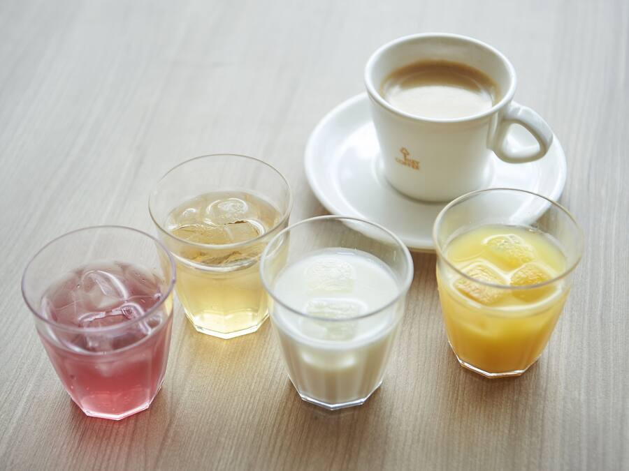 Ett bord med fyra glas med olika drycker och en kopp kaffe.