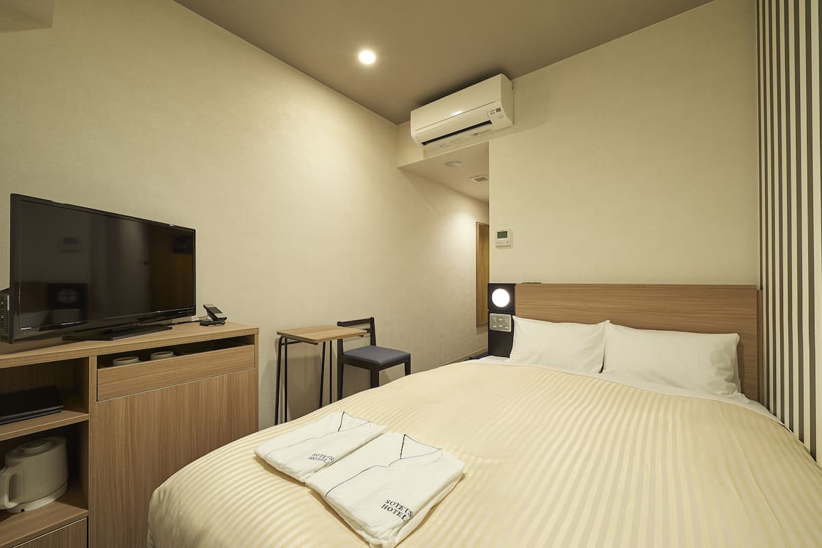 Een hotelkamer met een bed, een televisie, een bureau en een koffiezetapparaat.