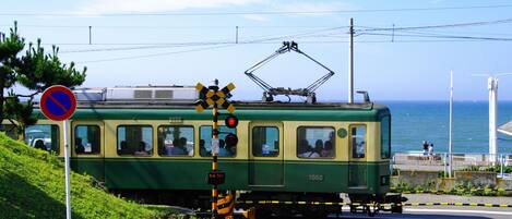 Un tranvía verde con pasajeros, una señal de prohibido estacionar y un paso de tren.