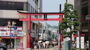 A busy urban street with a red torii gate, storefronts, and pedestrians.