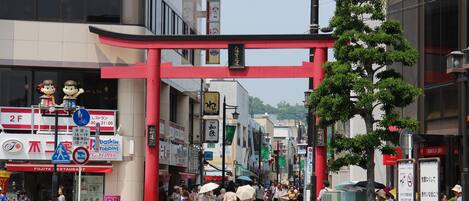 A busy urban street with a red torii gate, storefronts, and pedestrians.