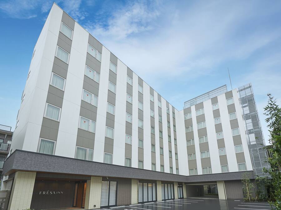 Ein modernes Hotelgebäude mit flacher Fassade, zahlreichen Fenstern und einem Parkplatz davor.