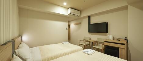 A hotel room with two beds, a desk, a chair, a TV, and a coffee maker.