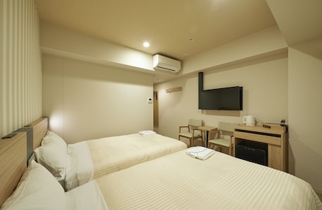 A hotel room with two beds, a desk, a chair, a TV, and a coffee maker.