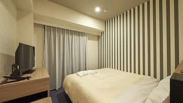 Una habitación de hotel con una cama, un escritorio con computadora, televisión y pared a rayas.