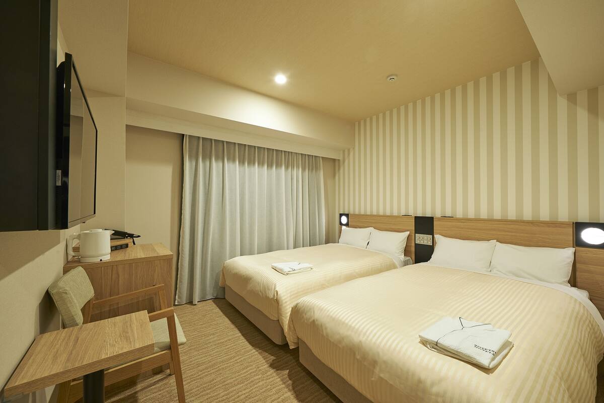 Een hotelkamer met twee bedden, een bureau, een stoel, een flatscreen televisie en een raam met gordijnen.