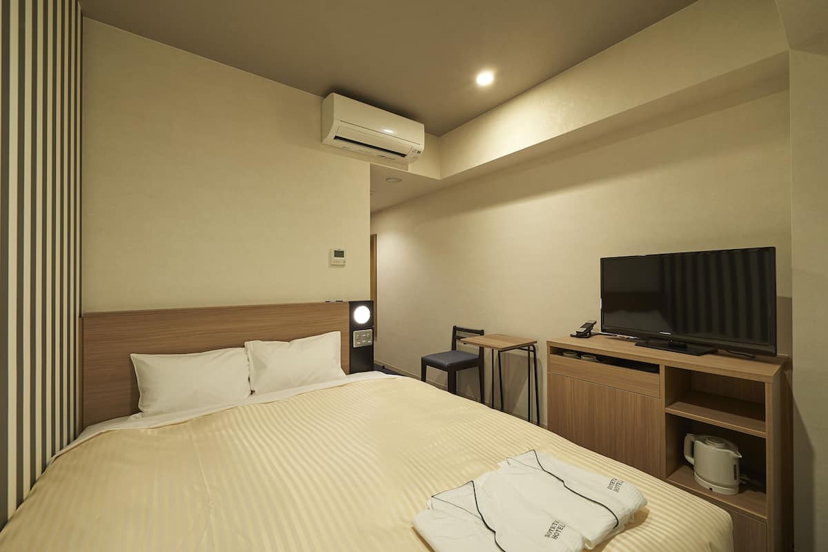 Een hotelkamer met een bed, een televisie, een bureau en een koffiezetapparaat.