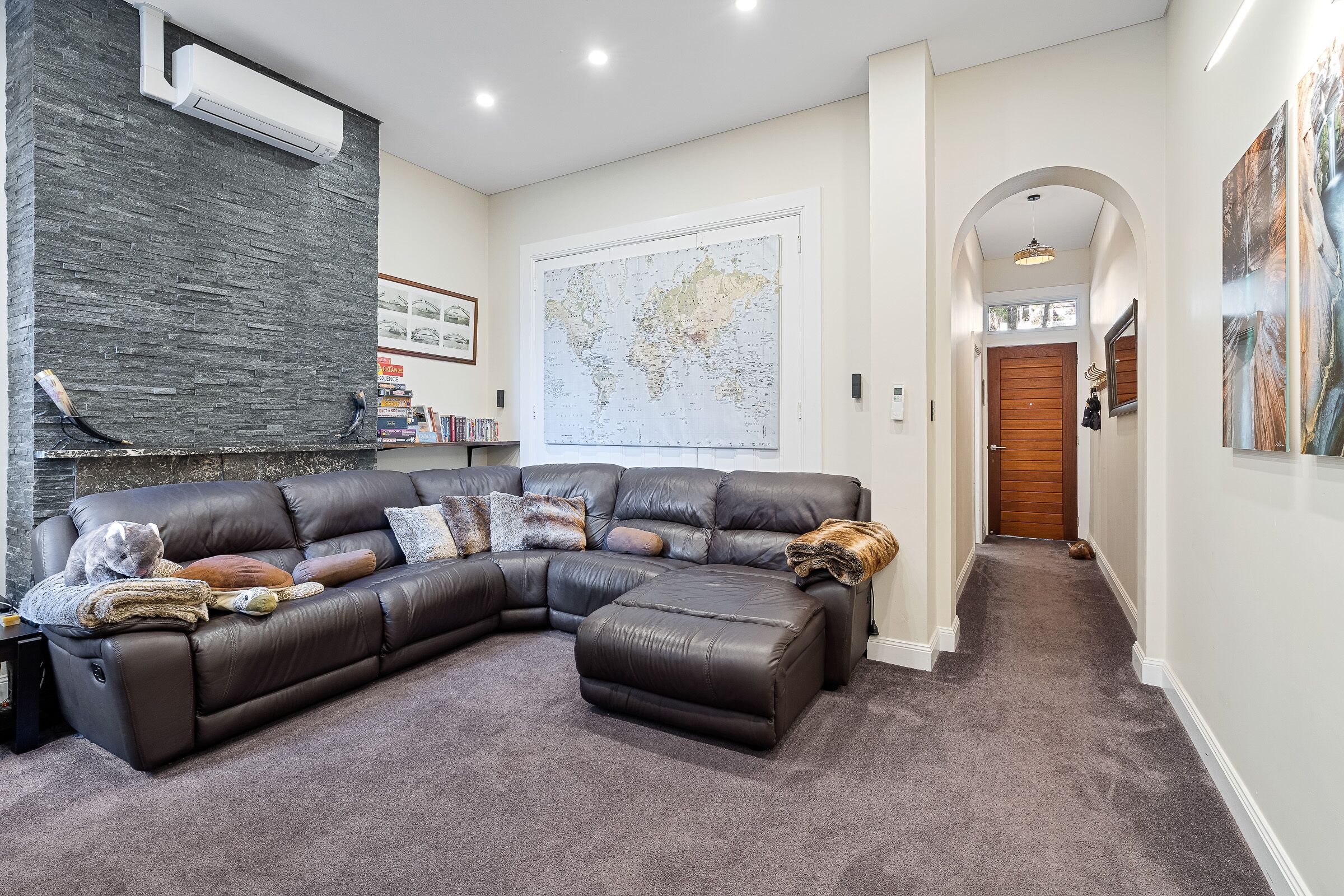 A living room with a sectional sofa, a large world map on the wall, and a hallway leading to a wooden door.