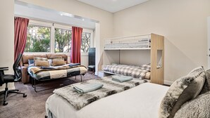 Un dormitorio con una cama grande, una cama más pequeña, un escritorio y una silla. Hay una ventana con cortinas y vistas a árboles.