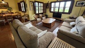 Un salon spacieux avec un grand canapé beige, une table basse en bois, des fauteuils en osier et un téléviseur.