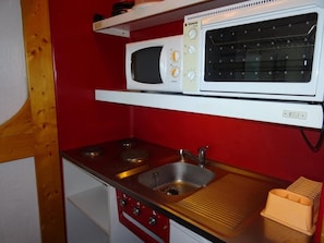 Een kleine keuken met een magnetron, fornuis en wastafel.