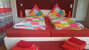 Een hotelkamer met een bed, voorzien van kleurrijke kussens, een rode sprei en een rood kleed.