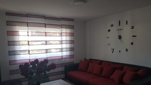 Een woonkamer met een rode bank, een witte salontafel met een boek en een bloevas, en een wandklok.