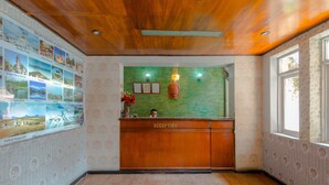 A reception area with a wooden reception desk, a green wall with framed pictures, and a window with patterned wallpaper. - Hotel River Holiday Inn (Kathmandu)