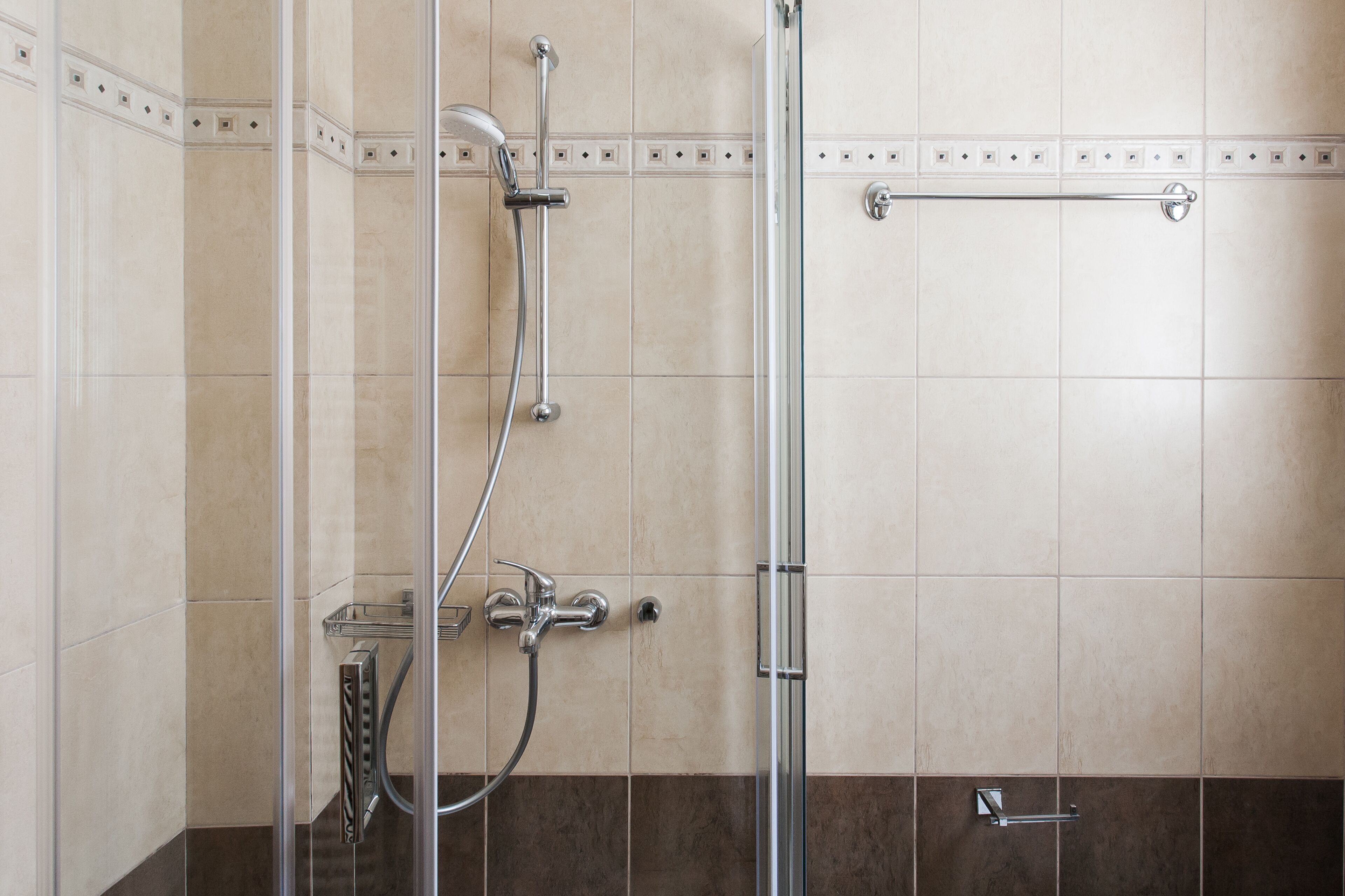 A modern shower with a glass enclosure, chrome fixtures, and a tiled wall with a decorative border.