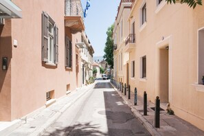 Une rue étroite bordée d’immeubles, avec des balcons et un ciel dégagé.
