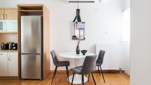 Ett modernt kök med ett kylskåp i rostfritt stål, träskåp, ett vitt matbord med fyra grå stolar och en hänglampa.