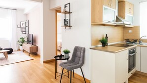 Ett modernt kök med träskåp, en inbyggd ugn och en liten matplats med en stol och ett bord.