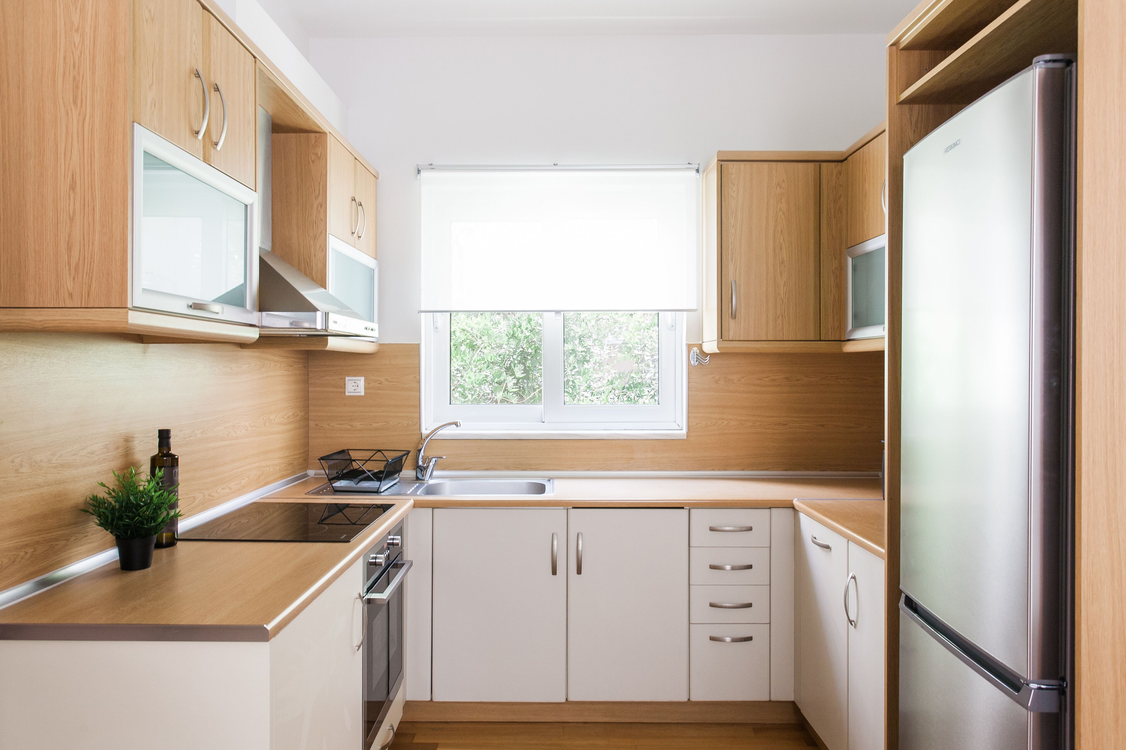 A modern kitchen with wooden cabinets, a stainless steel refrigerator, and a window providing natural light.