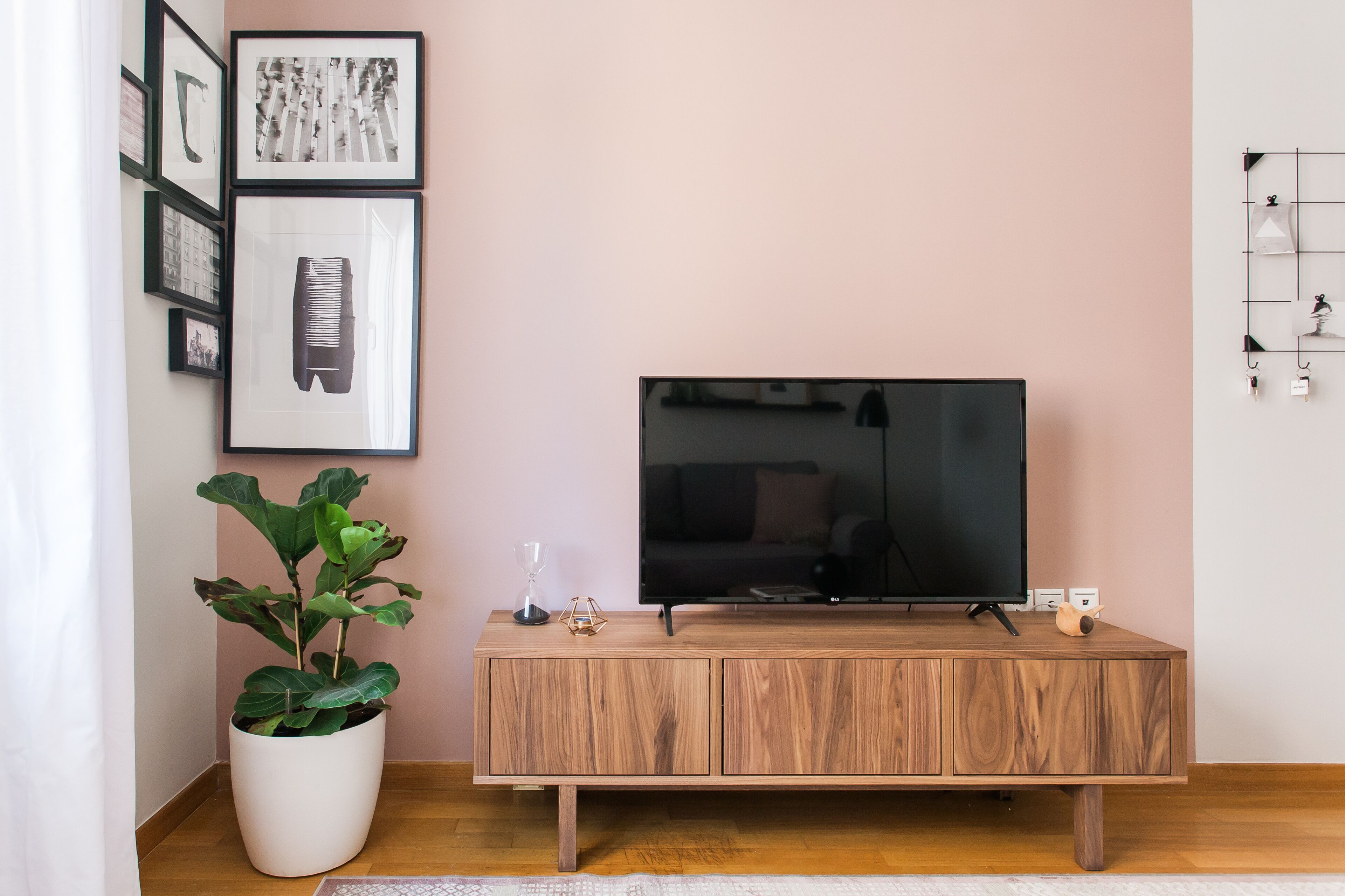 A living room with a wooden TV stand, a large flat-screen TV, a potted plant, and framed pictures on the wall.