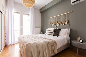 Une chambre à coucher avec un lit, une table de chevet, une décoration murale en macramé et une fenêtre avec des rideaux.