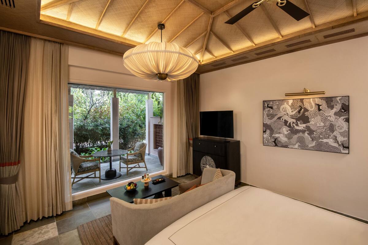 A modern hotel room with a large bed, a flat-screen TV mounted on the wall, a fireplace, and a dining area with a table and chairs.
