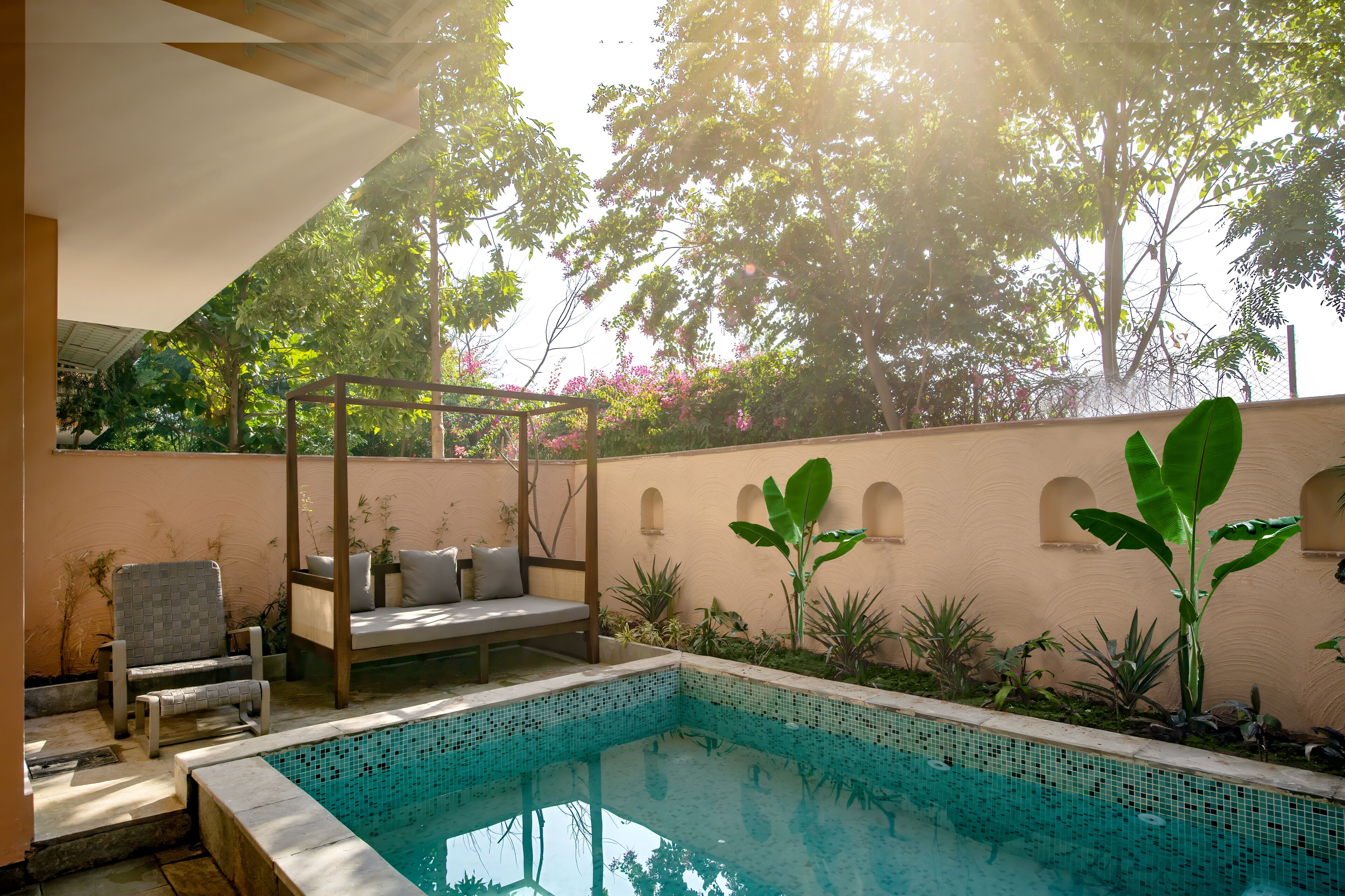 Zona de piscina con área de descanso, pérgola y vistas a árboles y flores.