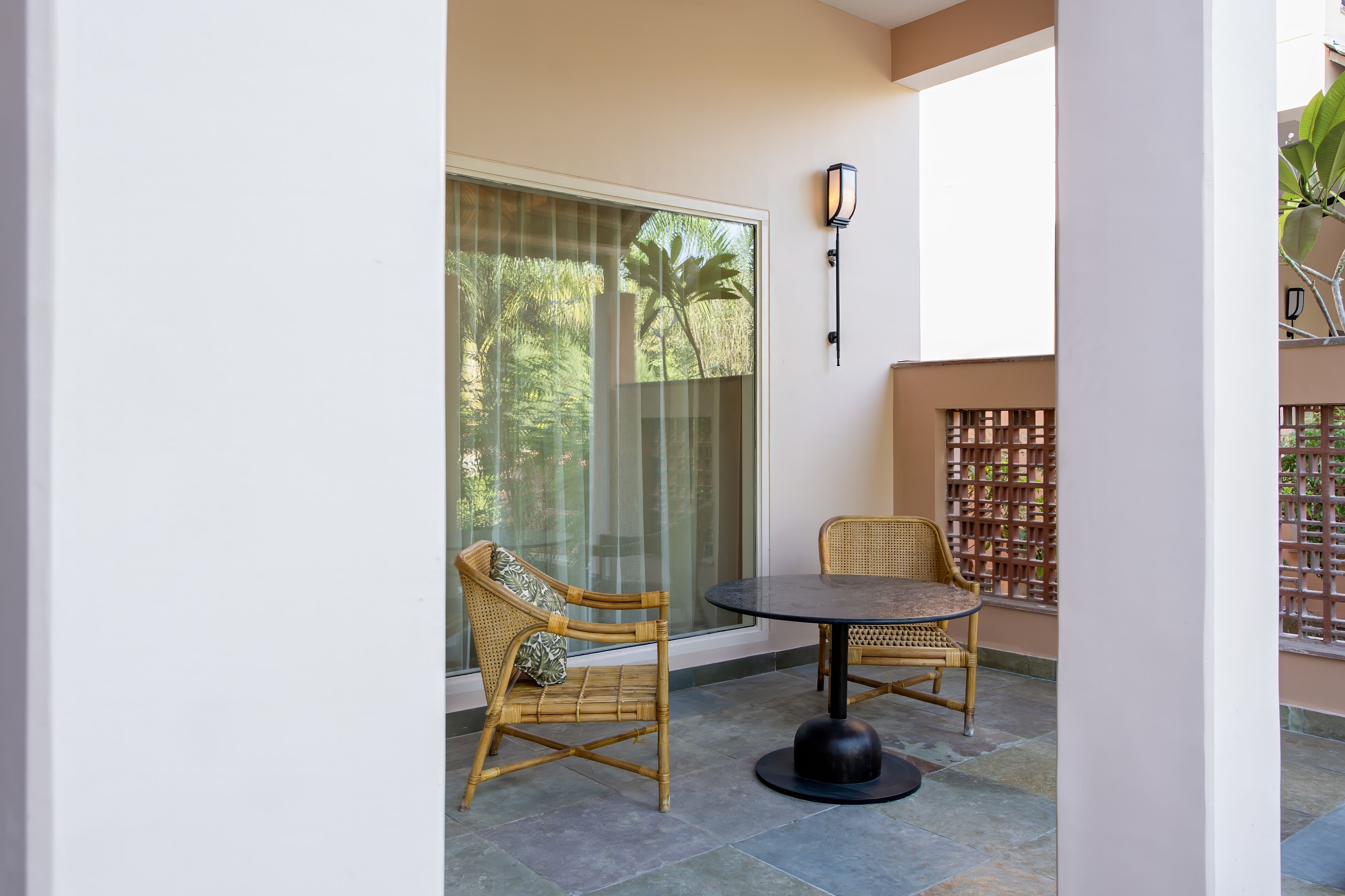 A balcony with wicker chairs, a round table, and a glass door leading to a garden.