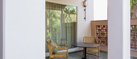 A balcony with wicker chairs, a round table, and a glass door leading to a garden.