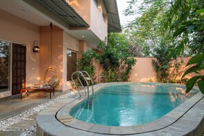 Una piscina con solárium de piedra, una silla de mimbre y una lámpara colgante.
