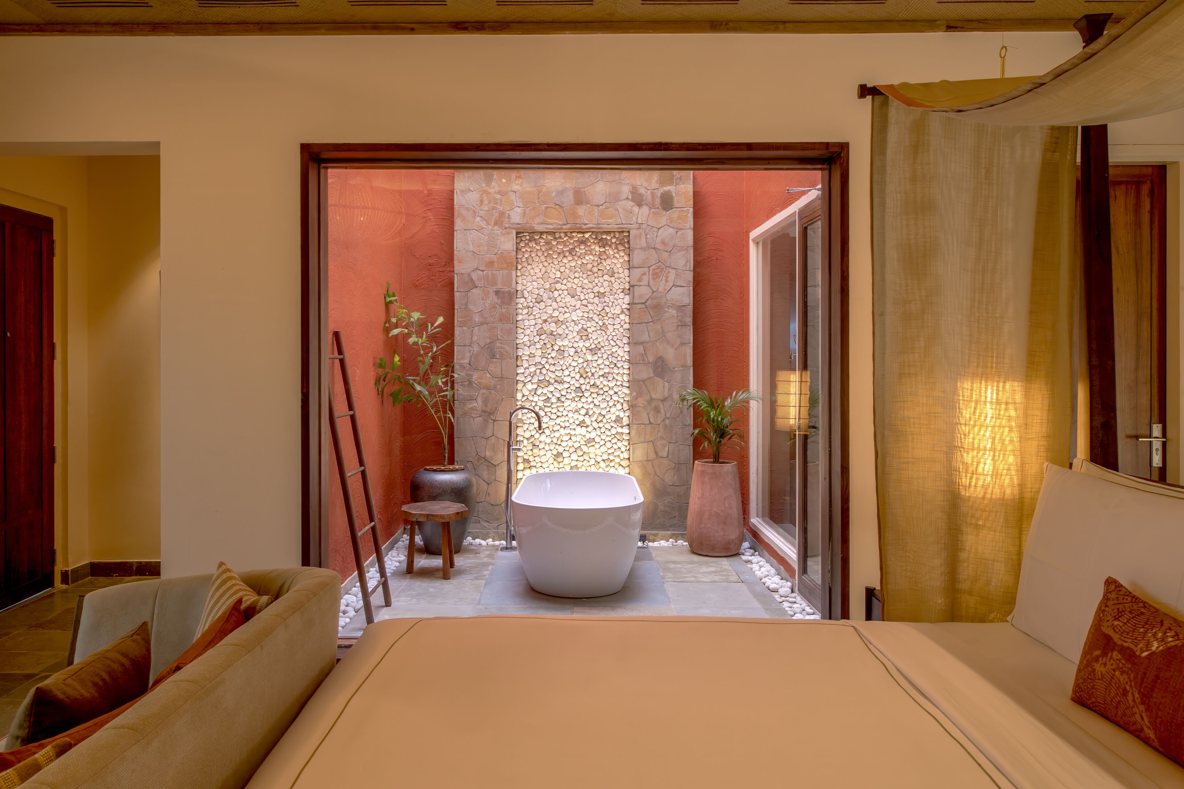 Une salle de bain moderne avec une baignoire sur pieds, un mur en pierre et une porte en verre donnant sur un balcon.
