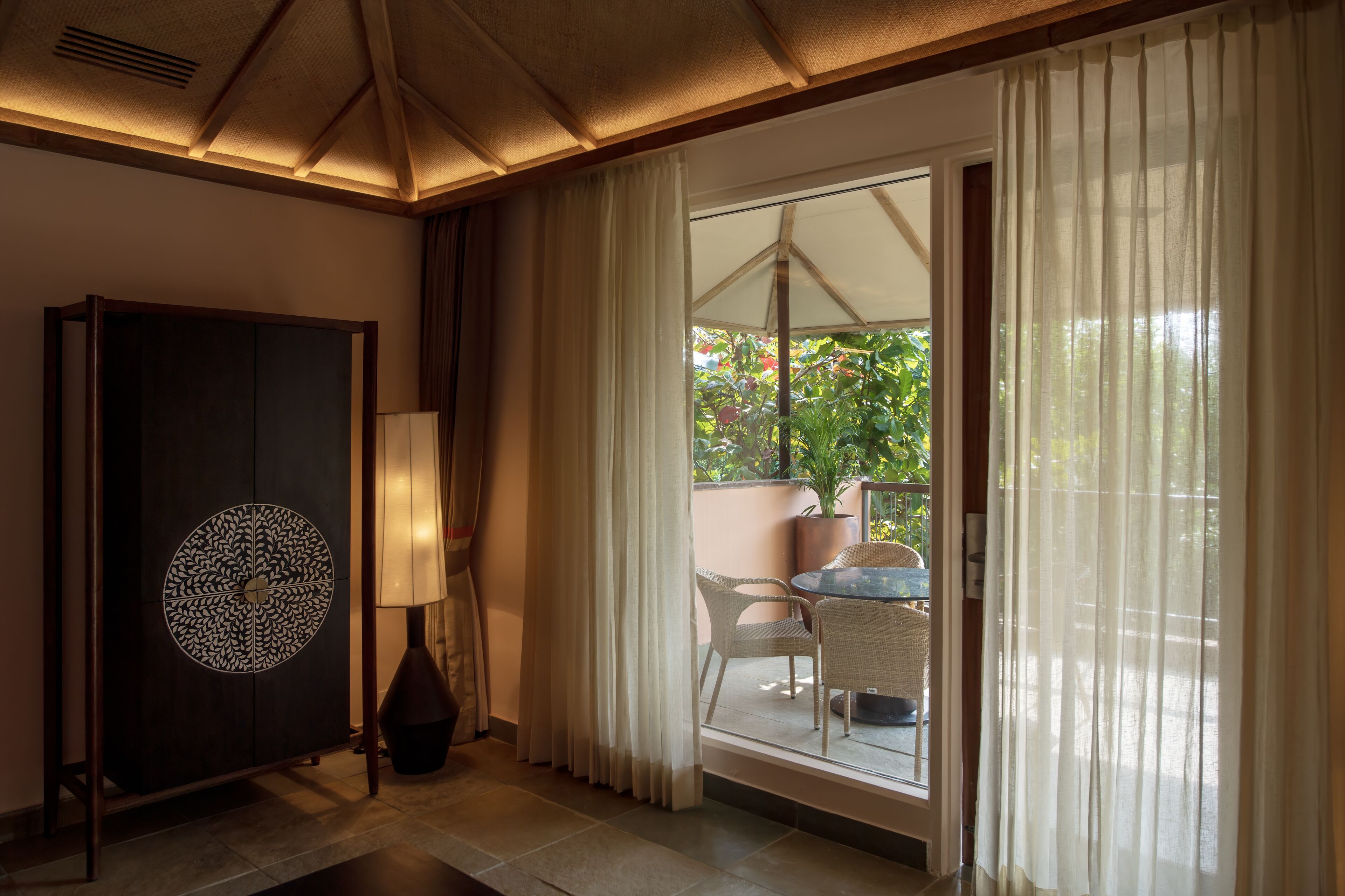 Una habitación con un ventanal grande, vistas al verdor exterior, un comedor con sillas y una mesa, y un mueble decorativo con un diseño circular.