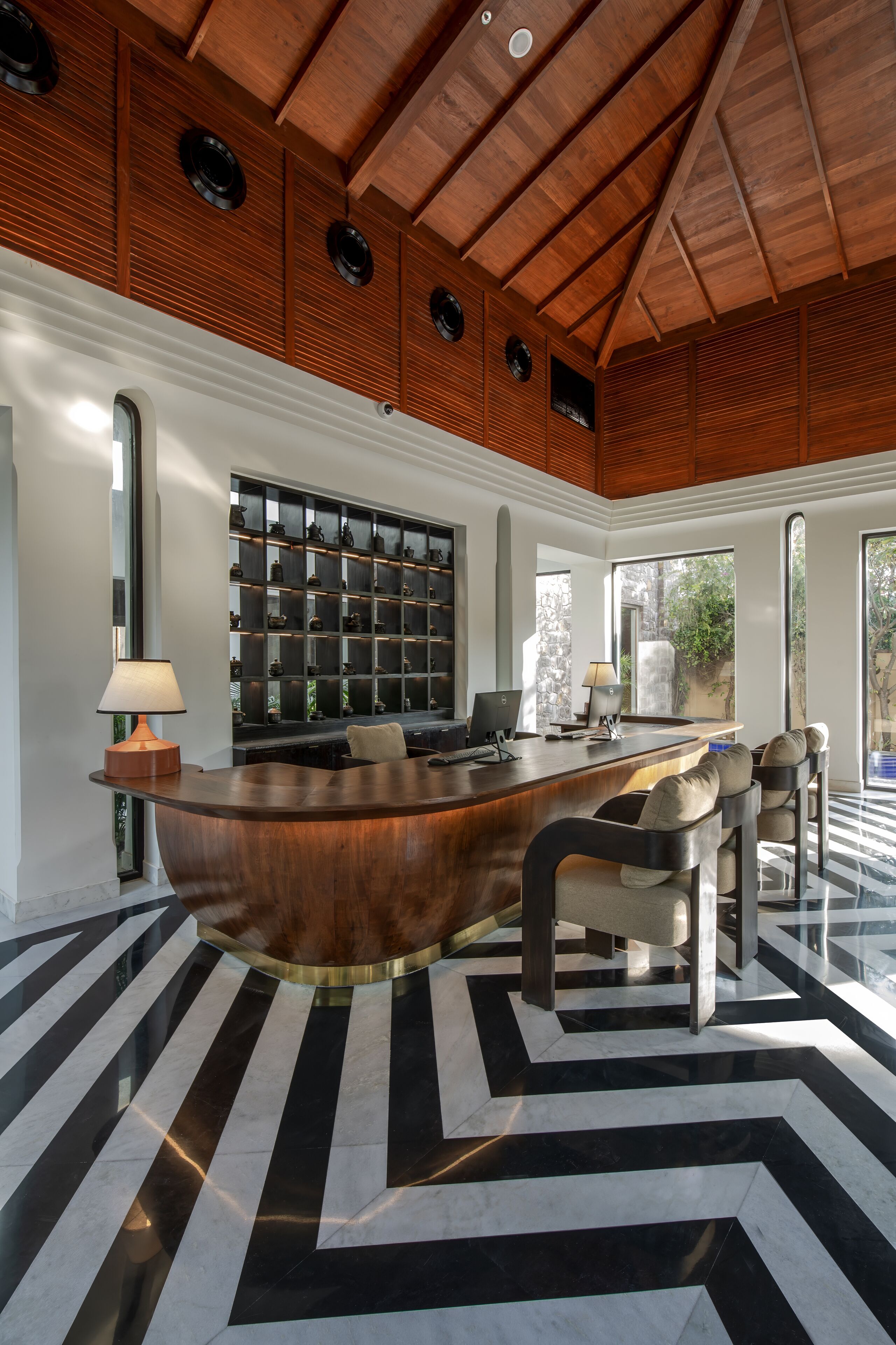 A modern interior with a curved wooden reception desk, a black and white patterned floor, and a large wall of shelves with various items.