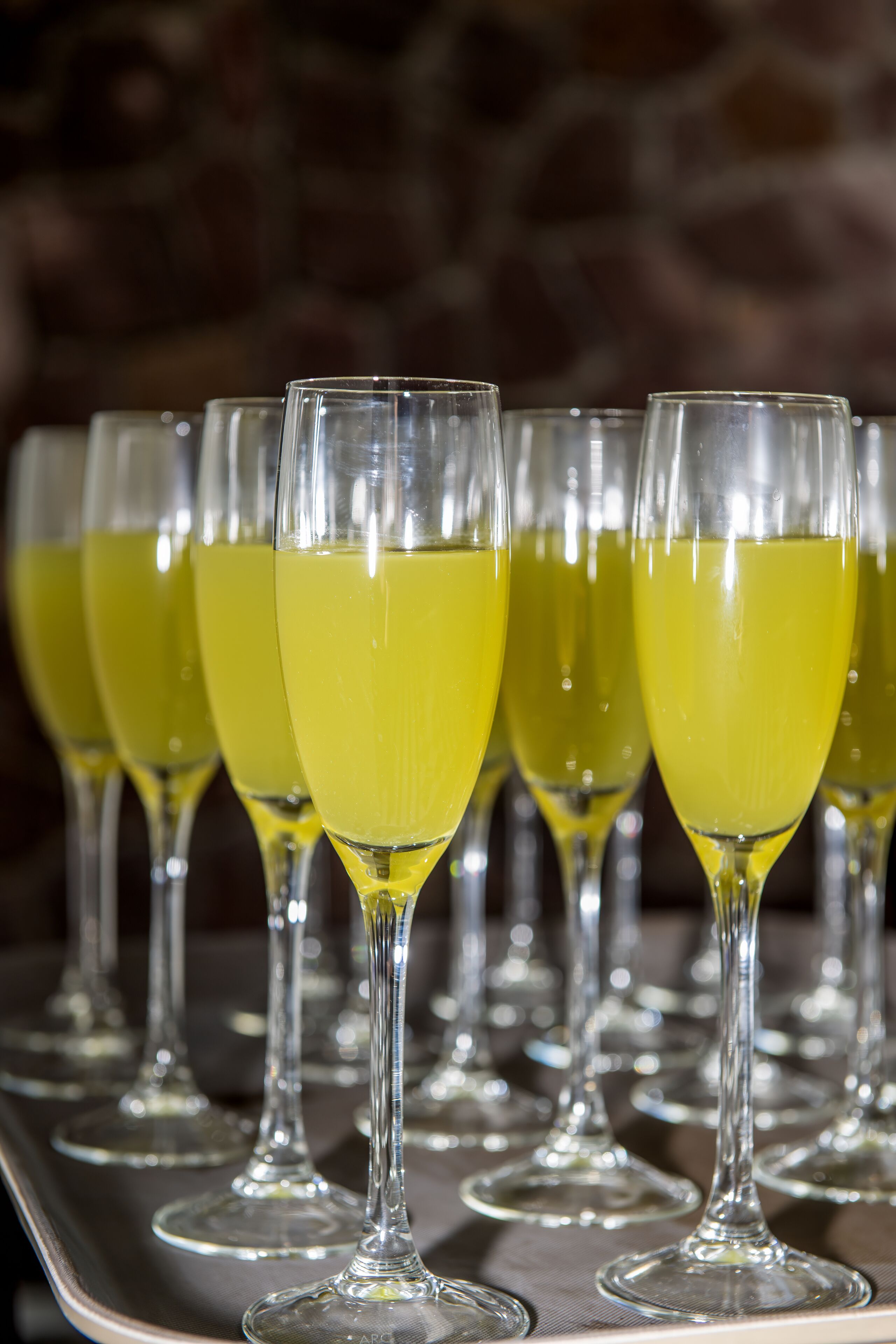A row of champagne flutes filled with yellow liquid, likely champagne, on a tray.