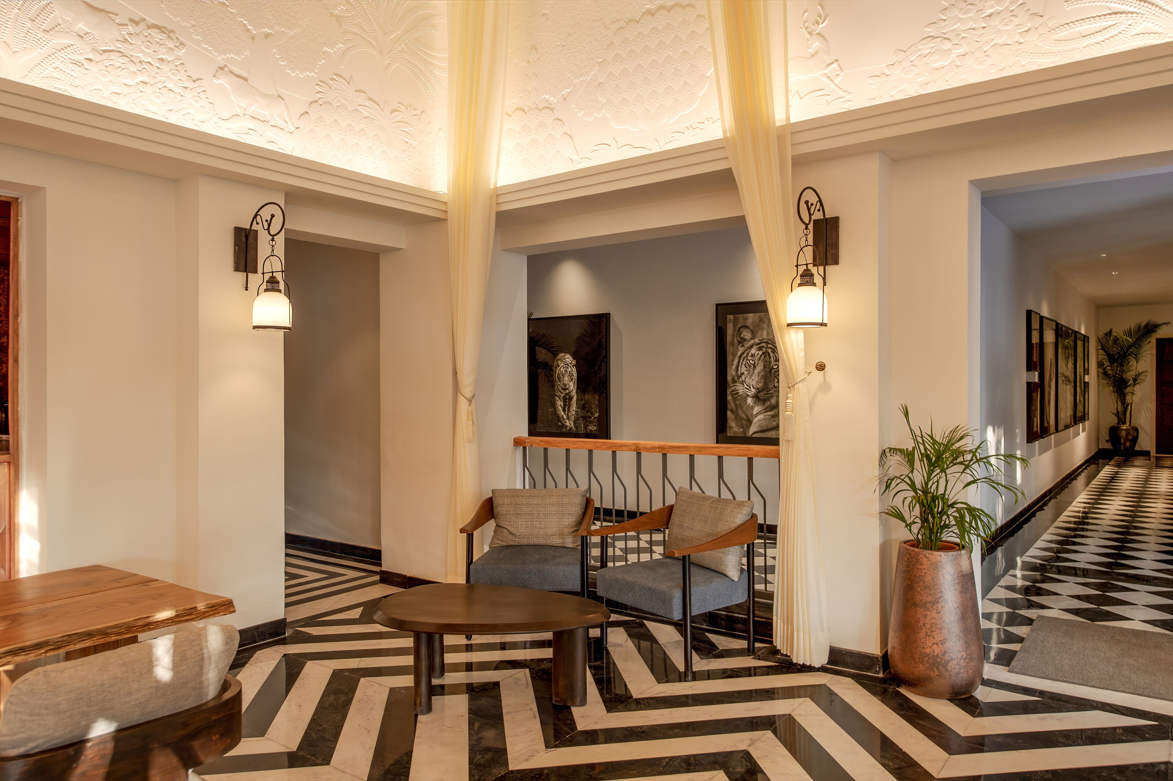 A lobby with a checkered floor, two armchairs, a wooden table, and a large potted plant.