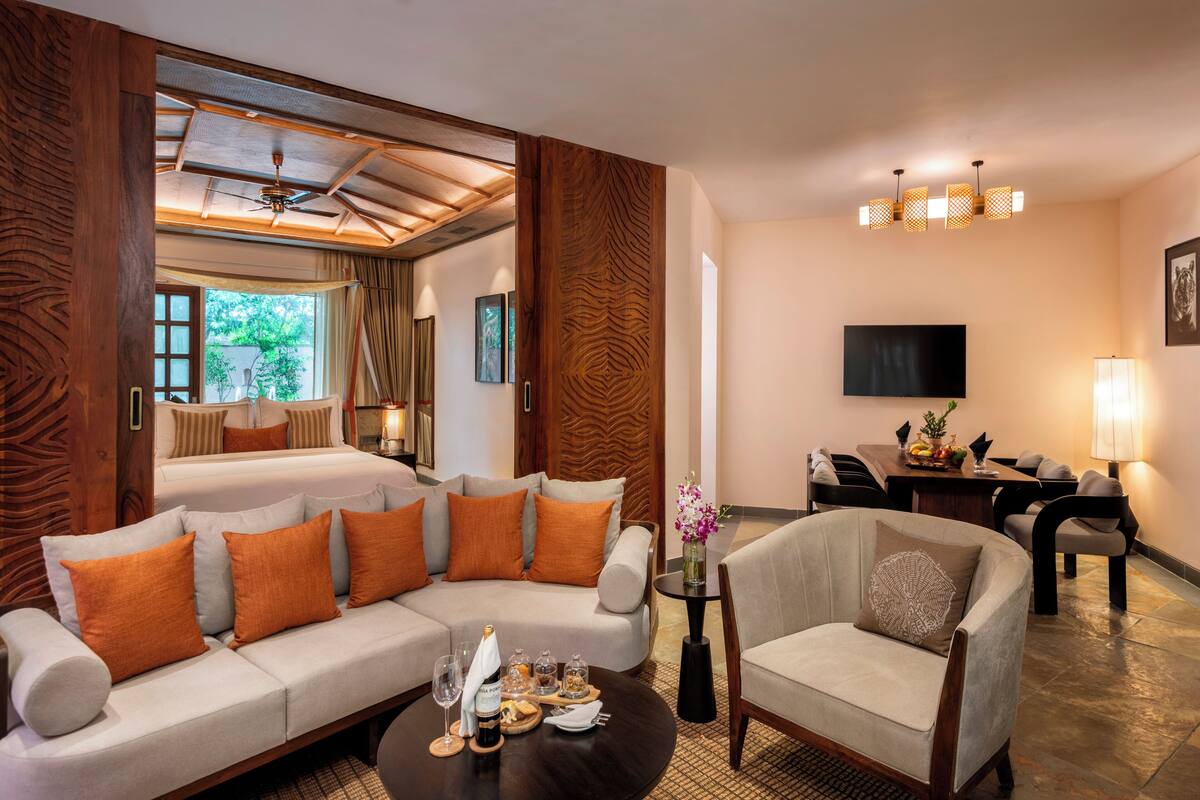 A hotel room with a sofa, armchairs, a dining table, and a TV.