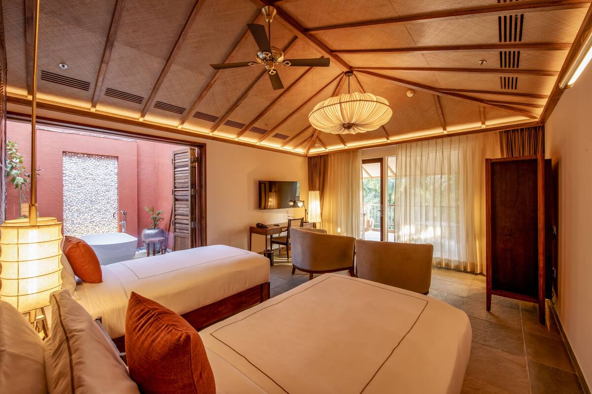 A hotel room with a bed, a desk, a chair, a ceiling fan, and a large window.