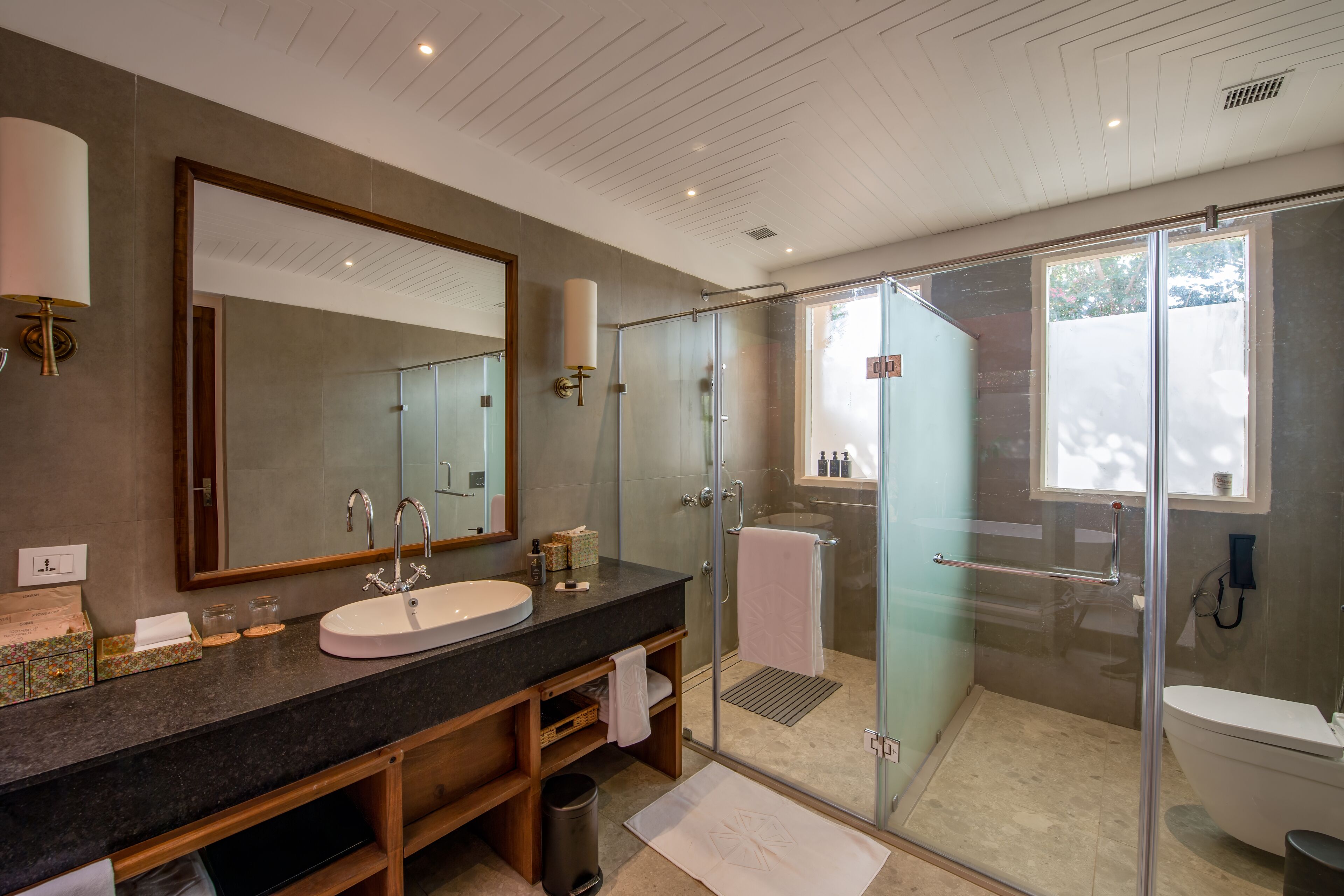 A modern bathroom with a large mirror, a sink, a glass shower enclosure, and a toilet.