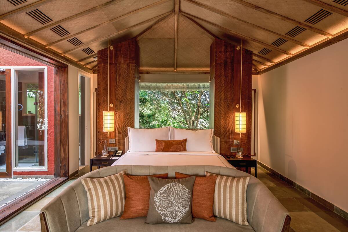 A spacious bedroom with a large bed, two bedside tables, and a view of greenery through a window.