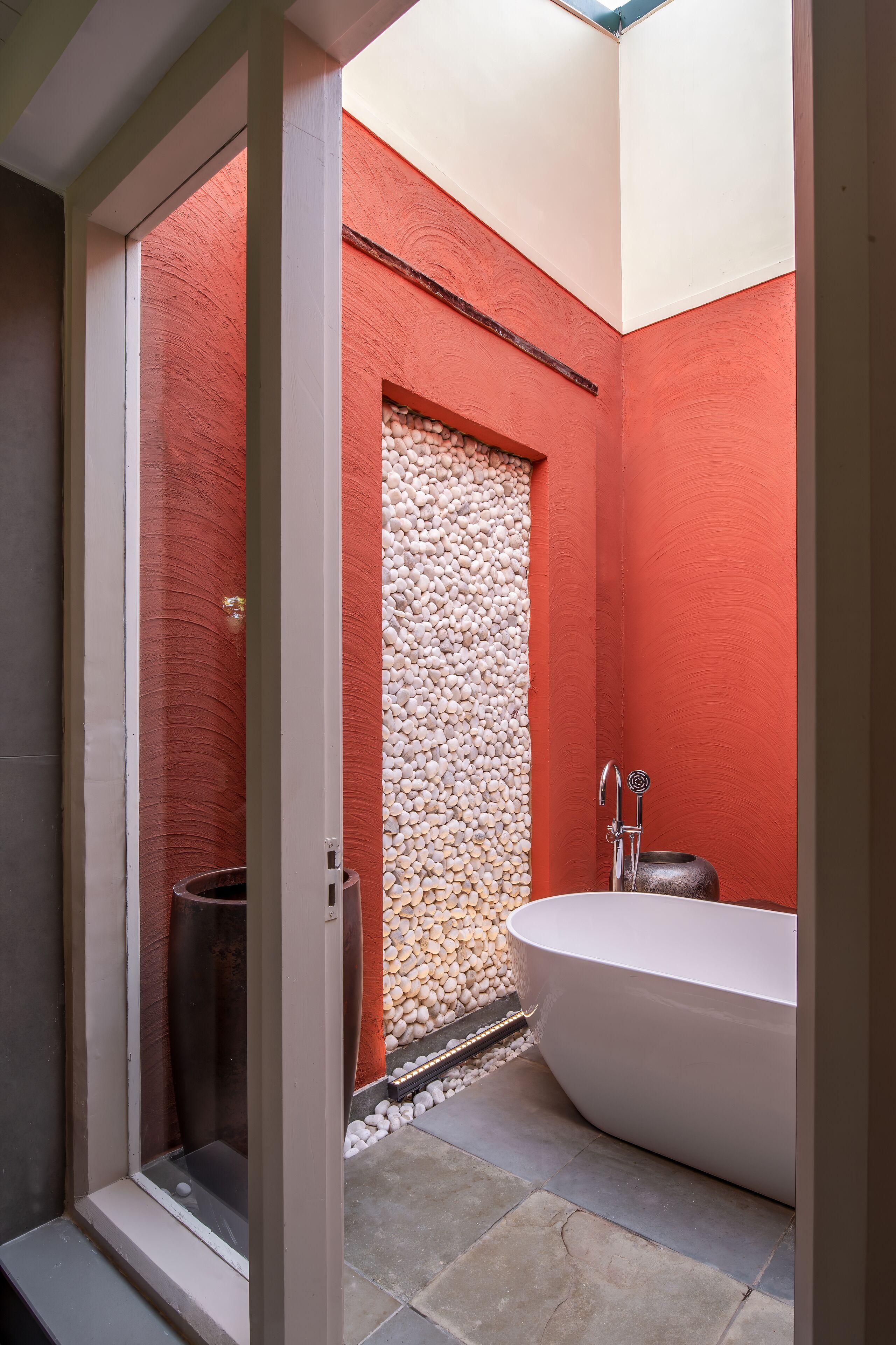 A modern bathroom with a freestanding bathtub, a shower with a pebble wall, and a glass-enclosed shower area.