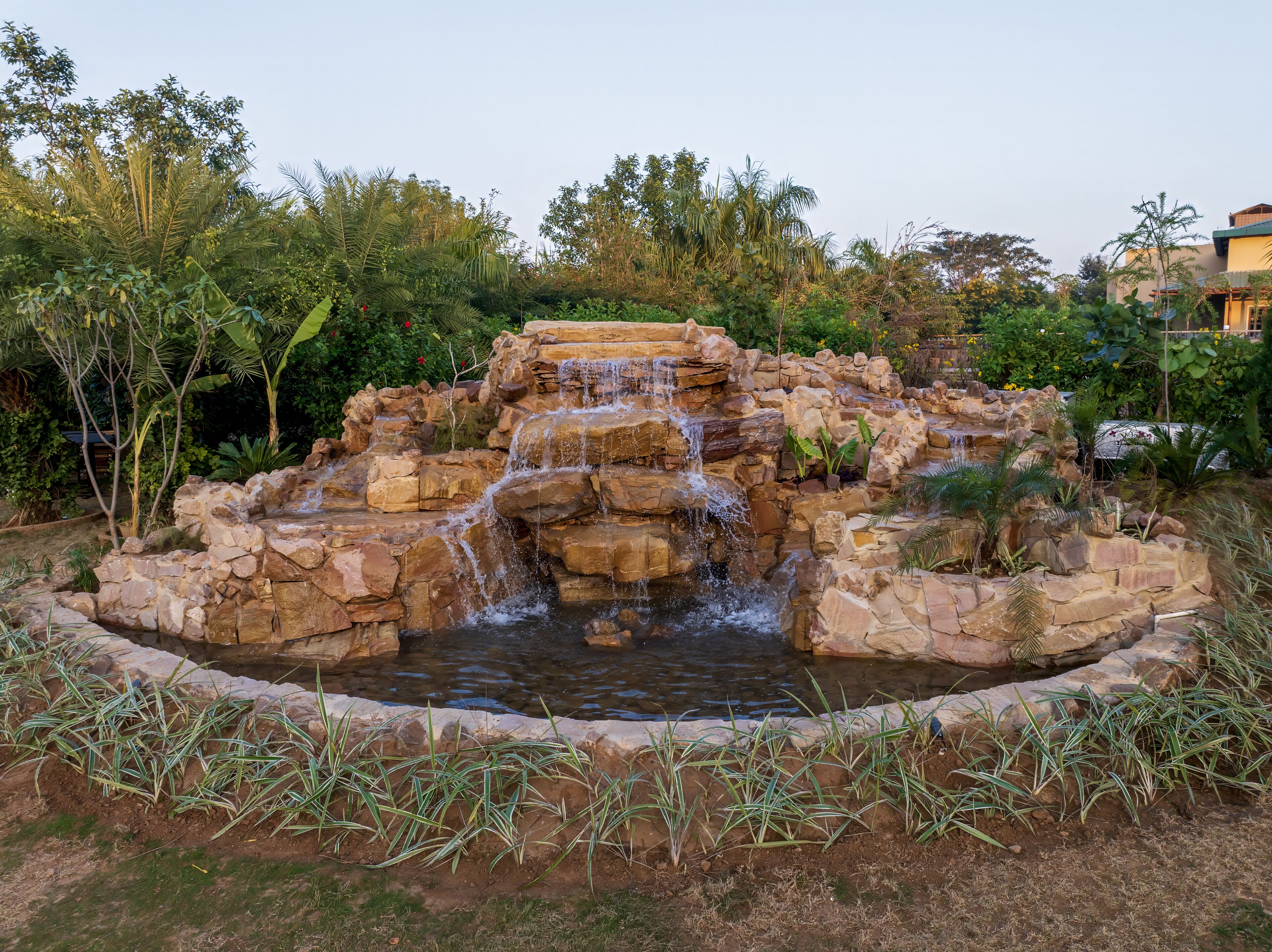 A naturalistic water feature with cascading water over rocks, surrounded by lush vegetation.