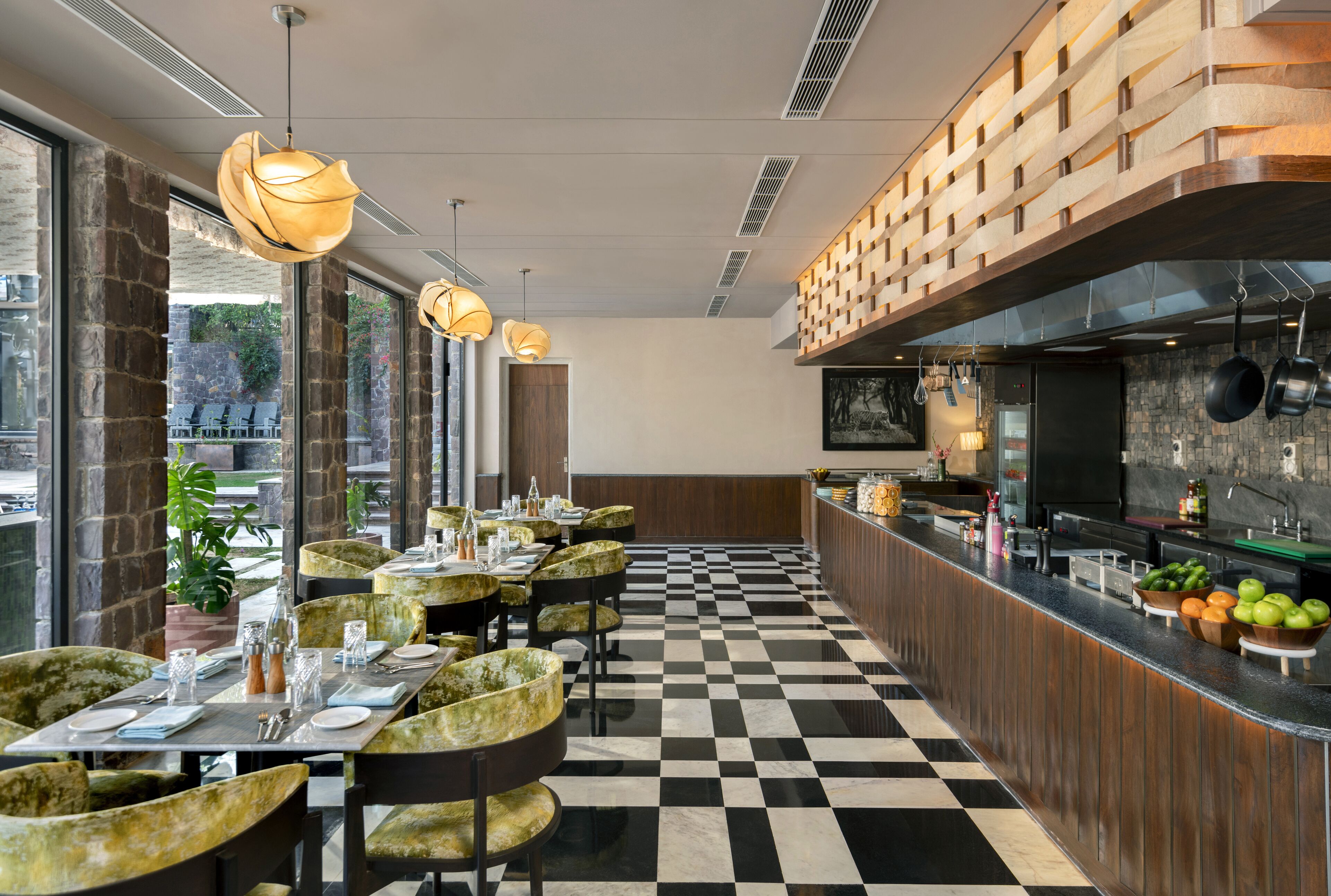 Ein Restaurant mit Schachbrettfußboden, runden Tischen mit grünen Stühlen und Pendelleuchten.