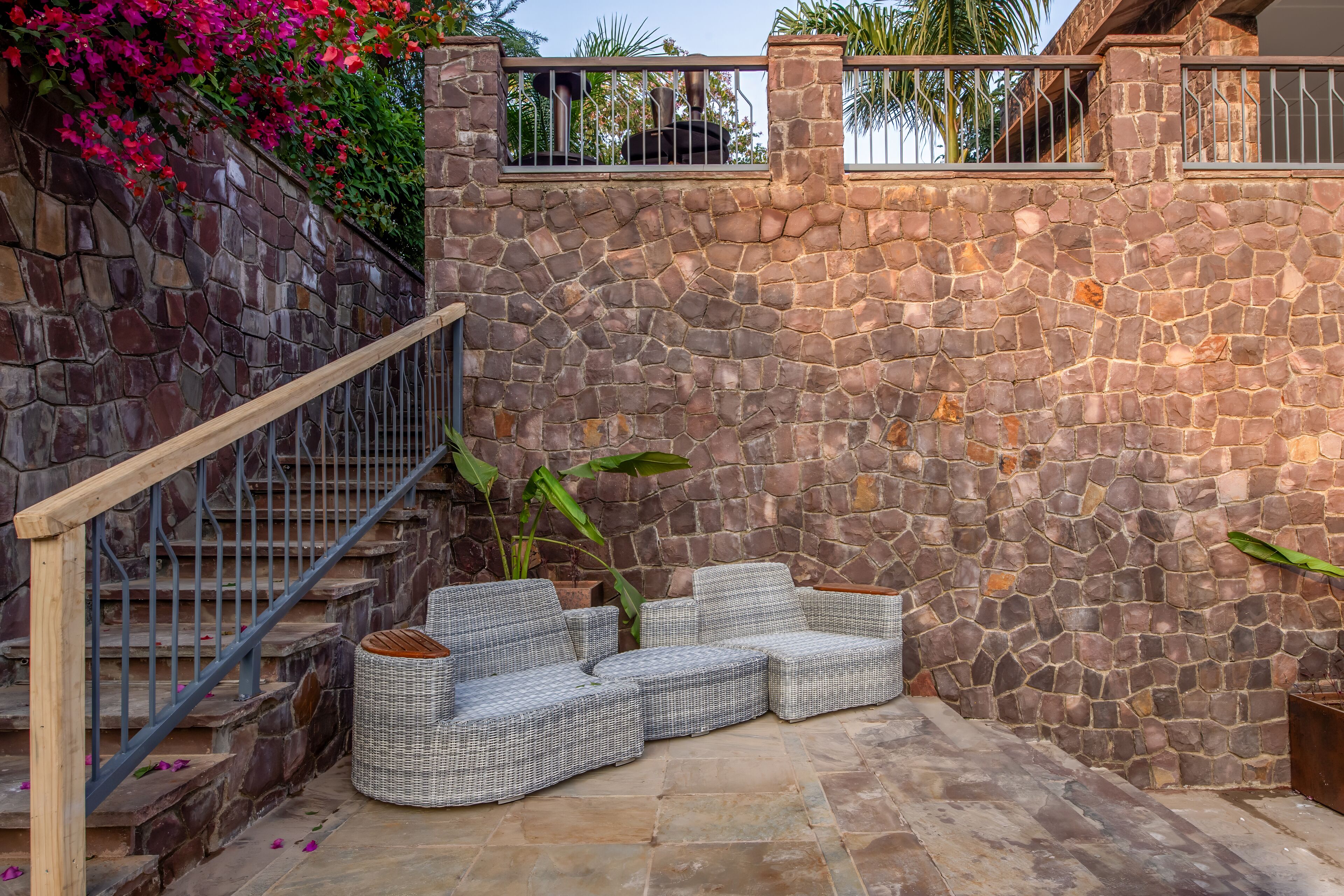 A stone wall with a staircase, a wicker sofa, and a potted plant.