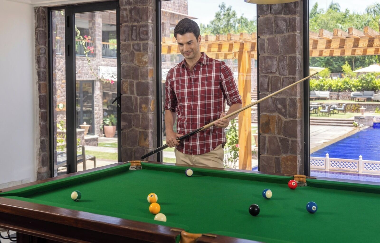 A pool table with a person playing, a pool table, and a view of a pool outside.