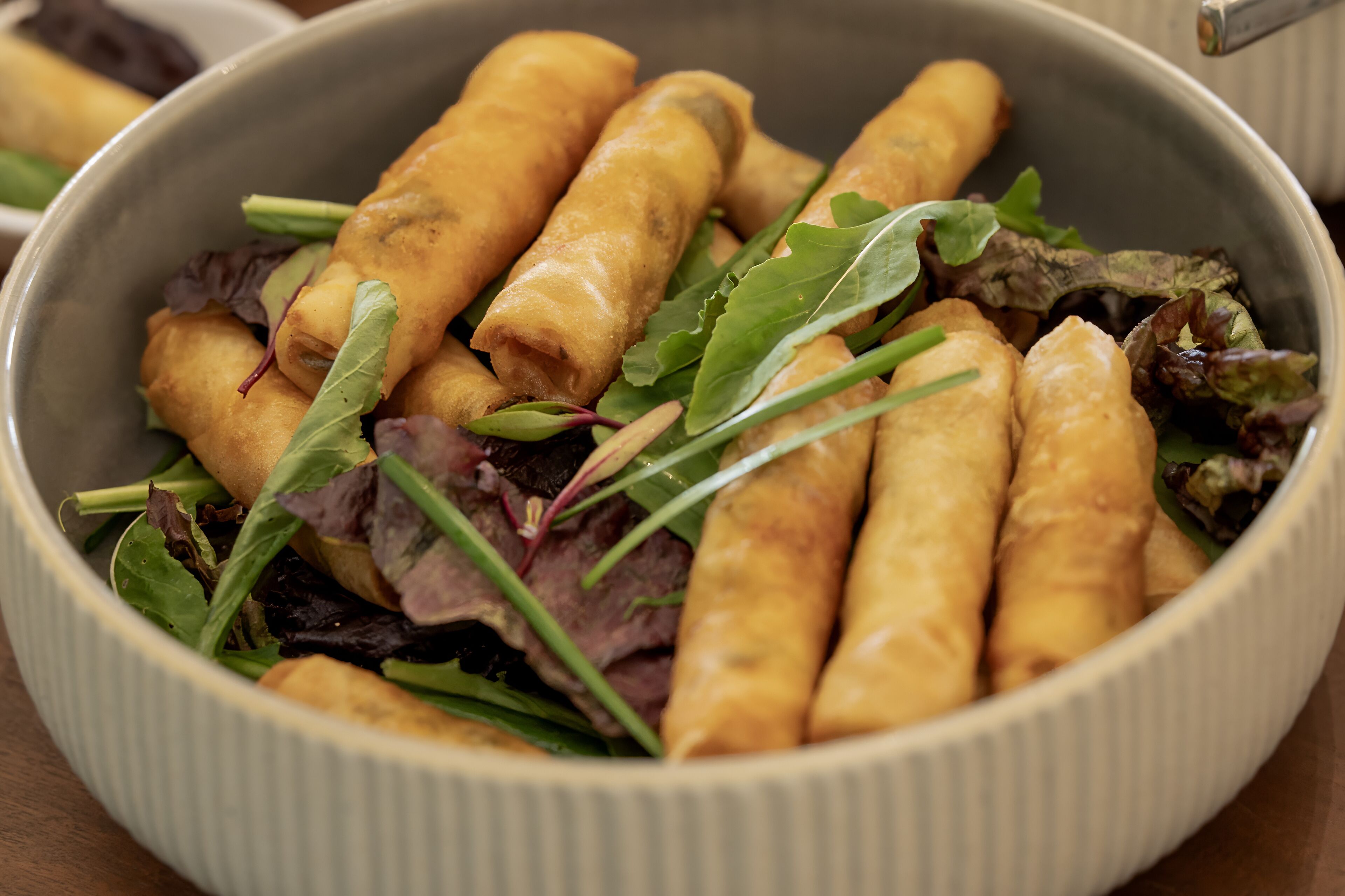 A bowl of spring rolls with greens.