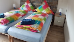 Ein Bett mit bunter Decke und Kissen, ein hölzernes Kopfende, ein Nachttisch mit Lampe und Holzboden.