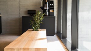 A modern reception area with a wooden reception desk, a coffee machine, and a potted plant.