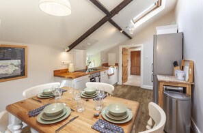 A dining area with a wooden table set for four, a kitchen in the background, and a modern refrigerator. - Stockham Farm, Dulverton (Dulverton)