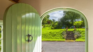 Una porta verda amb mànega de metall que dona a una zona pavimentada amb una escala de pedra i un jardí ple de gespa i arbustos.