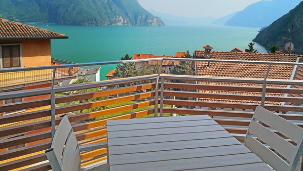 Een balkon met tafel en stoelen met uitzicht op een meer en bergen.